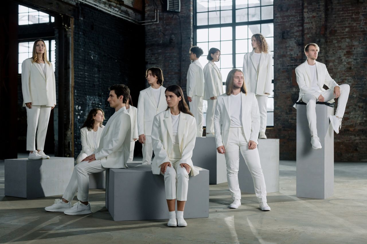 Diverse group of individuals in white clothing posing on platforms indoors with natural lighting.