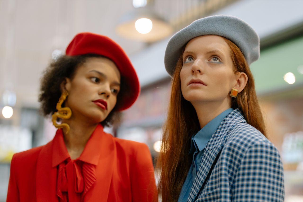 Two fashionable women wearing berets and trendy outfits indoors, embodying modern style.